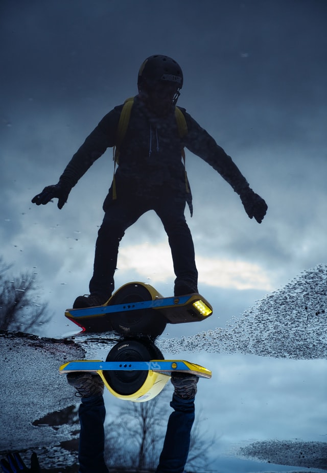 Guy posing on onewheel with puddle reflection