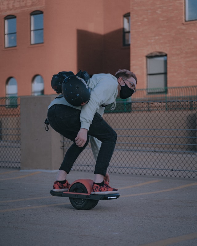 Guy riding onewheel pint touching board with gear on back